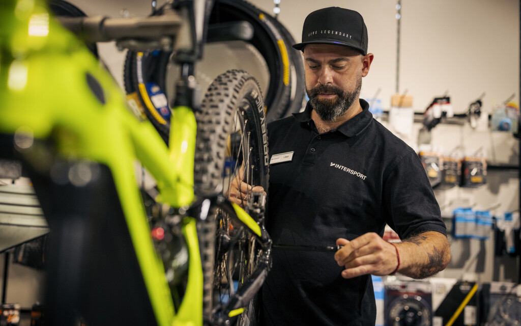 Ein Fahrradmechaniker wartet ein leuchtend grünes Mountainbike in einer professionellen Fahrradwerkstatt und stellt den Antrieb ein.
