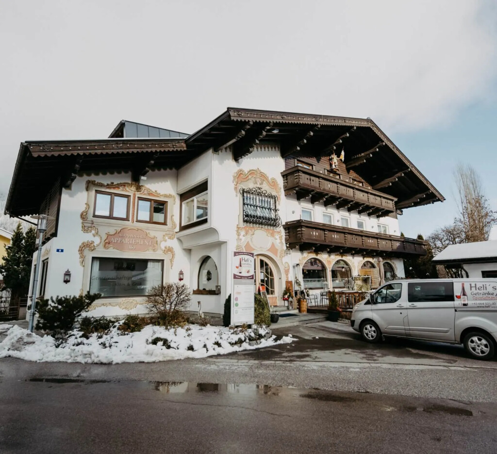 Traditionelles bayerisches Alpenhotel mit aufwendig bemalter Fassade, dunklen Holzbalkonen und Winterschnee.