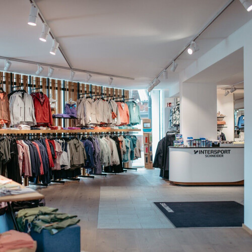 Helles Intersport-Geschäftsinterieur mit vielfältiger Sport- und Outdoor-Bekleidung an Kleiderständern sowie einem Kundenservice-Schalter.