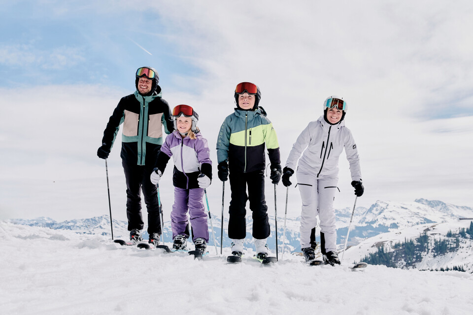 Eine vierköpfige Familie fährt auf einer verschneiten Skipiste Ski. Erwachsene und Kinder tragen Helme und komplette Skiausrüstung.