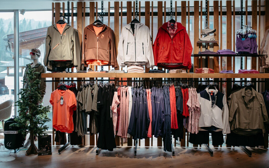 Modernes Ladeninterieur, das Outdoor-Bekleidung, Jacken, Hemden und Sportbekleidung auf Holzdisplays präsentiert.