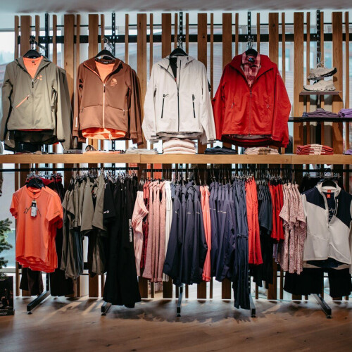 Modernes Ladeninterieur, das Outdoor-Bekleidung, Jacken, Hemden und Sportbekleidung auf Holzdisplays präsentiert.