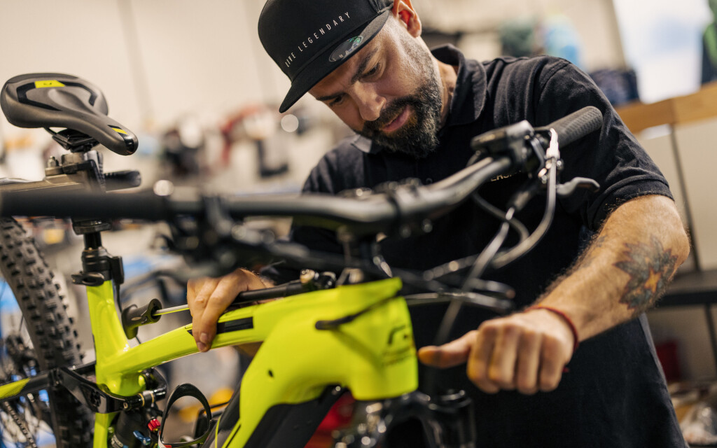 Ein bärtiger Fahrradmechaniker wartet ein leuchtend gelbes E-Mountainbike in einer professionellen Fahrradwerkstatt.