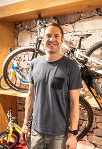 Lächelnder Mann in einem Fahrradgeschäft, stehend zwischen Mountainbikes und Kinderfahrrädern.