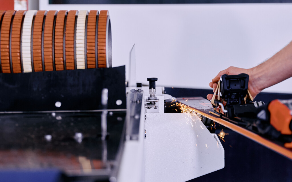 Eine Skikantenschleifmaschine sprüht Funken, während eine Hand einen Ski zum professionellen Tuning führt.