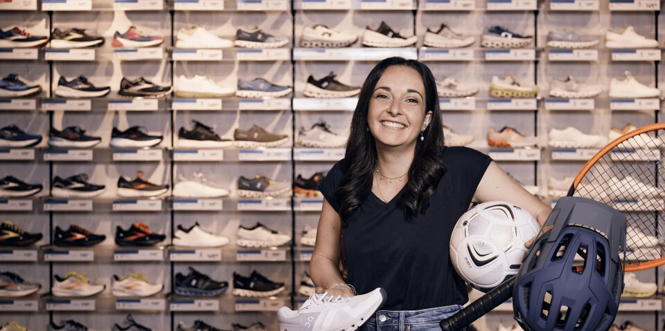 Lächelnde Frau hält einen weißen Sportschuh, Fußball, Helm und Tennisschläger in einem Schuhgeschäft.
